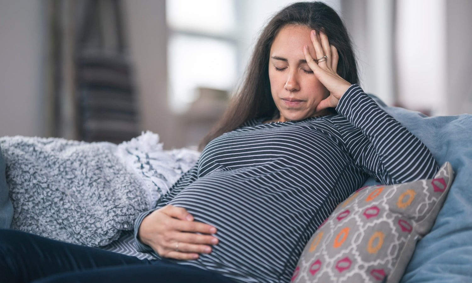 Raskaana oleva nainen pahoinvoivana, pitelee päätään ja vatsaansa väsyneenä - kärsii hyperemeesi oireista
