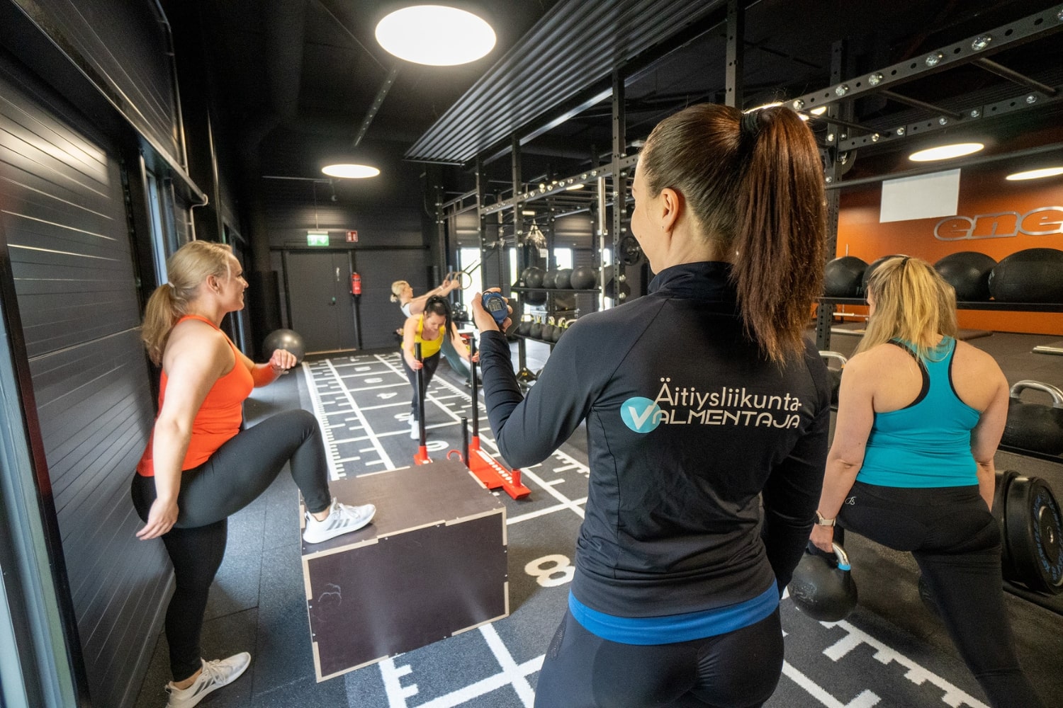 Ryhmä naisia voimaharjoittelun parissa, äitiysliikuntavalmentaja ohjaamassa.