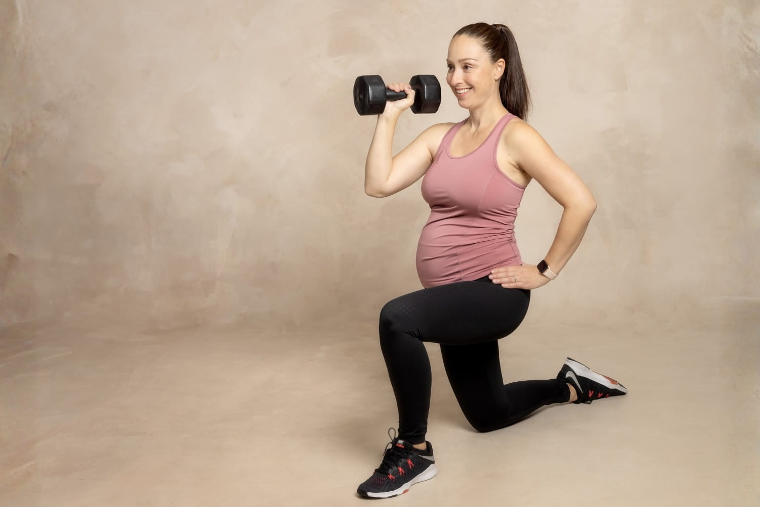 Raskaana oleva nainen tekemässä voimaharjoittelu, puolipolviasennossa, toisessa kädessä käsipaino. 