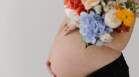 9Months-paketti raskaana oleville, kuvassa nainen pitelee raskausvatsaa ja toisella kädellä kukkia.